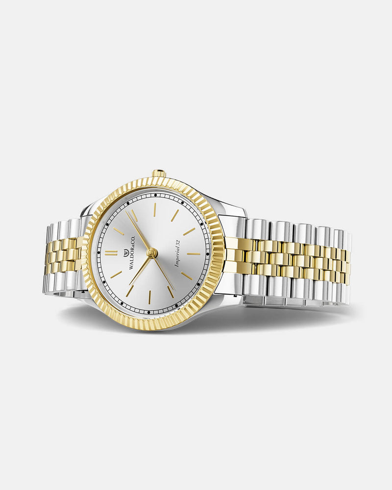 A round womens watch in silver and 22k gold from Waldor & Co. with silver sunray dial and a second hand. Seiko movement. The model is Imperial 32 Positano 32mm.