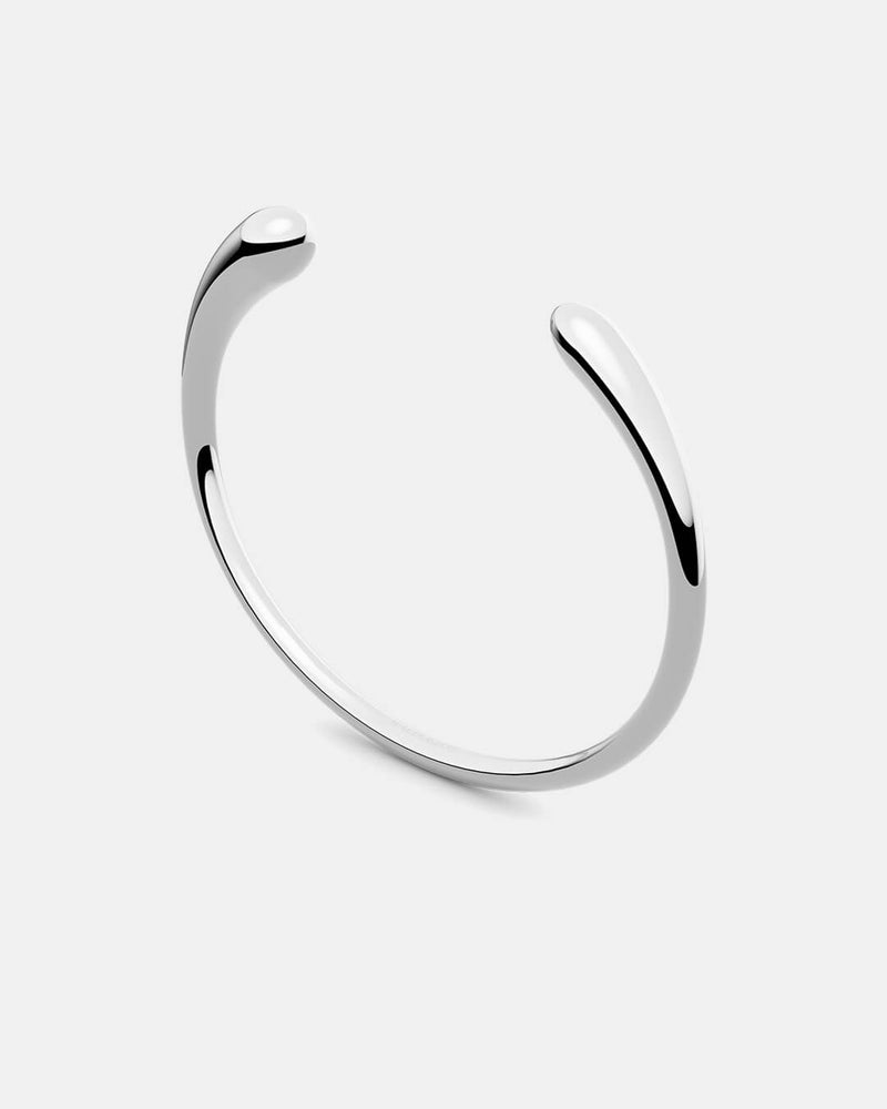A polished stainless steel bangle in silver from Waldor & Co. One size. The model is Teardrop Bangle Polished